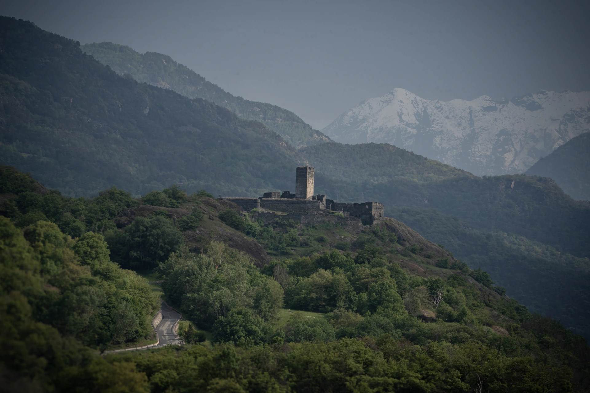 A stone castle surrounded by wooded slopes and distant mountains
