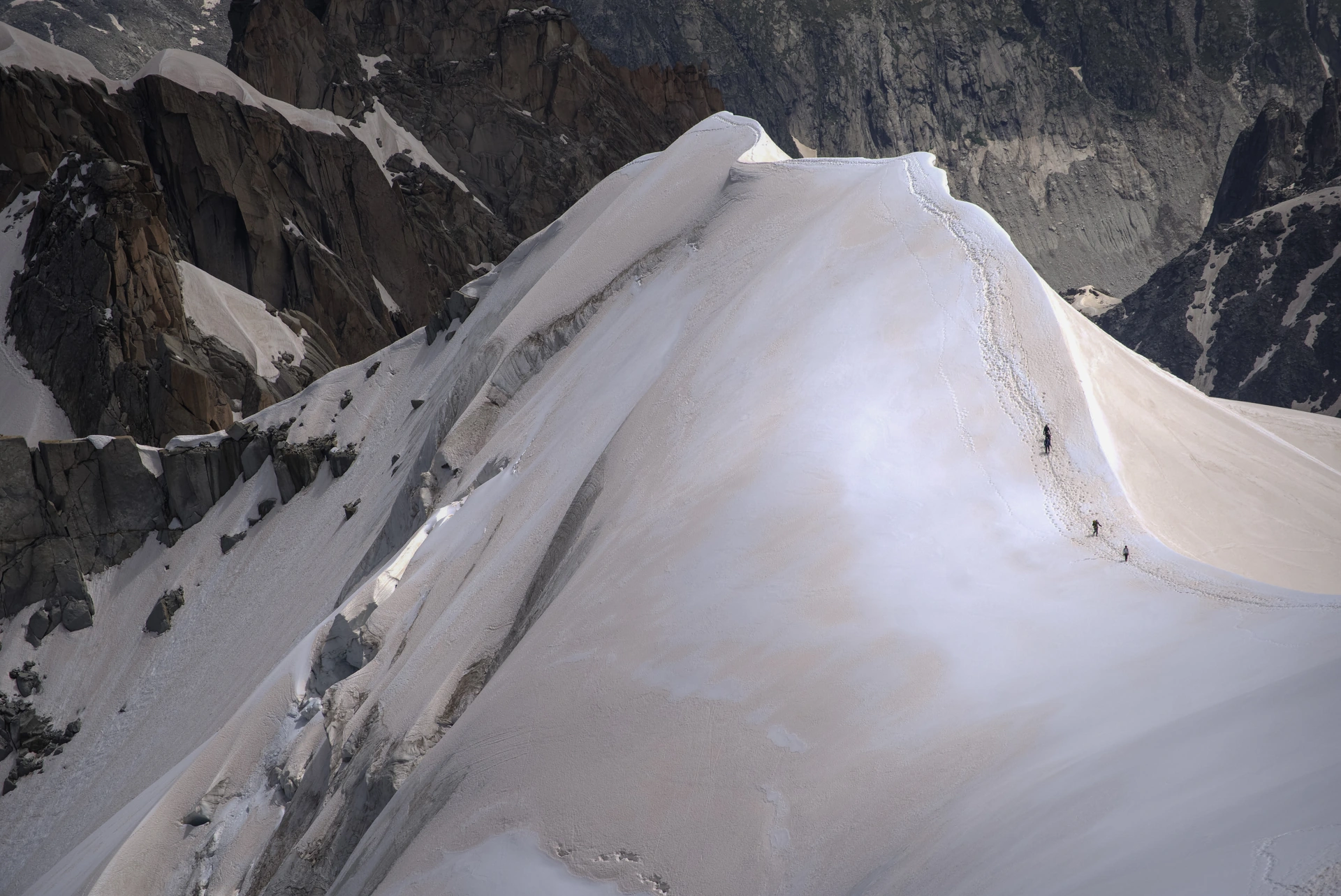 Walkers following a narrow snow ridge between mountain faces